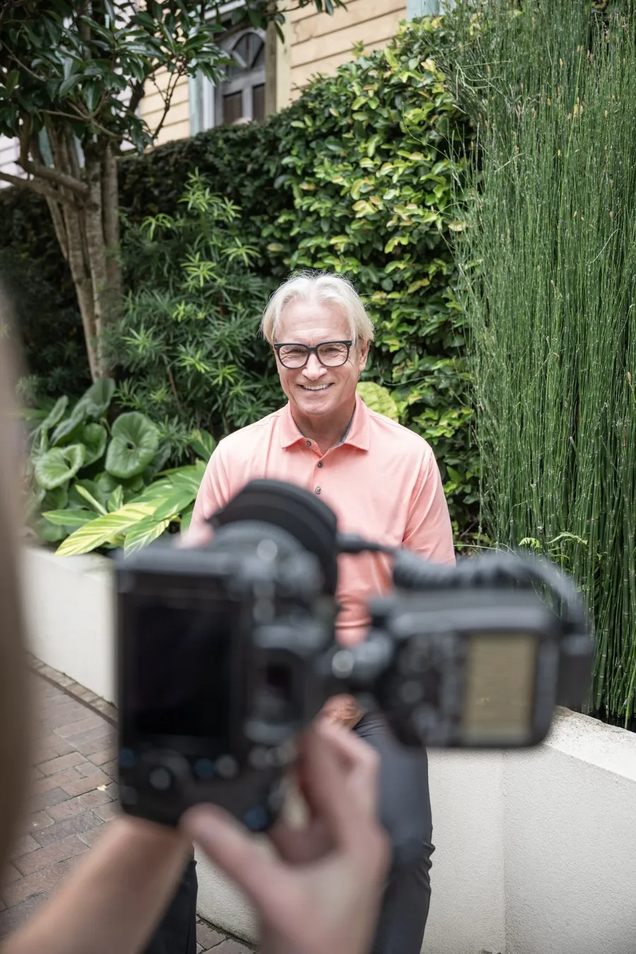 A smiling patient having his new smile photographed in the Beyond Exceptional Dentistry courtyard
